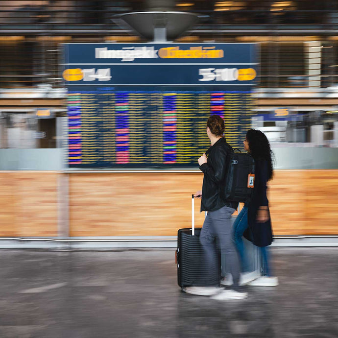 Two people with luggage standing in front of an airport information board.